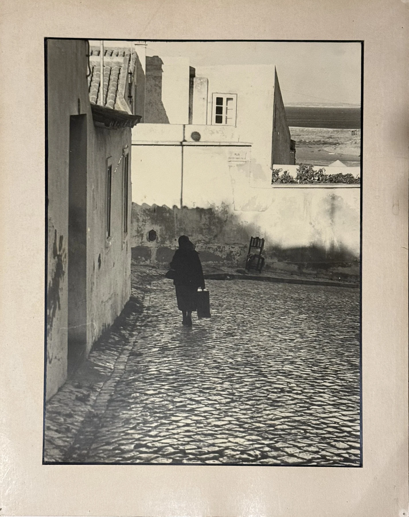 Eine einzelne dunkle Figur gibt einem hellen Platz seinen Maßstab. Das Pflaster führt den Blick zu den Mauern im Hintergrund.
